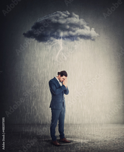 Pessimistic and depressed businessman standing under rain as the negative thoughts stands over his head like a storm cloud. Person suffering anxiety and headache. Concept for emotional crisis