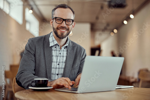 Cheerful bearded man using laptop in cafe