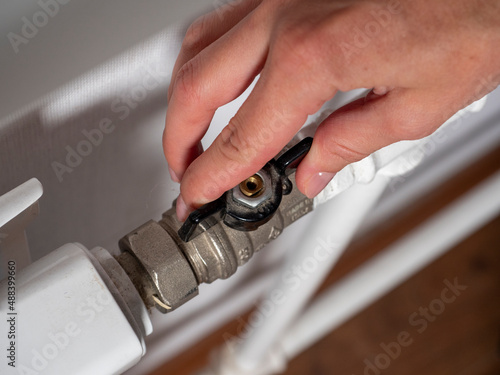 A woman's hand on the valve of the central heating battery. The concept of heat overlap, the crisis of energy carriers.