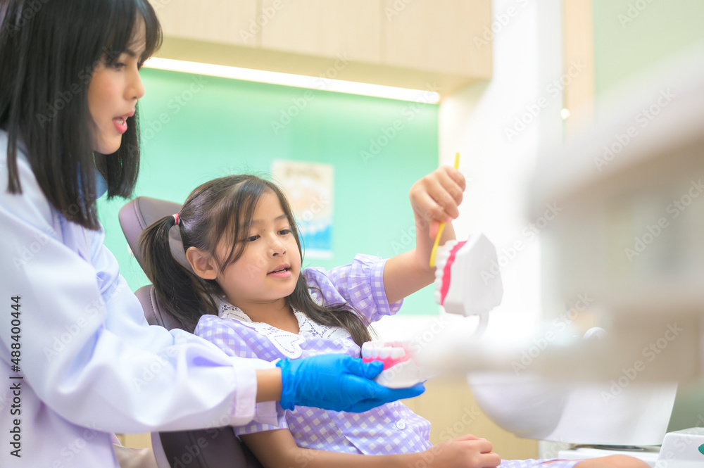 Female dentist demonstrating how to brush teeth to a little girl in dental clinic, teeth check-up and Healthy teeth concept Female dentist demonstrating how to brush teeth to a little girl in dental clinic, teeth check-up and Healthy teeth concept