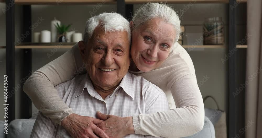 Close up portrait happy carefree pensioner couple, older wife and husband hugging smile look at camera. Spouses enjoy time together, laughing while having warm conversation, rest at home. Love concept Close up portrait happy carefree pensioner couple, older wife and husband hugging smile look at camera. Spouses enjoy time together, laughing while having warm conversation, rest at home. Love concept