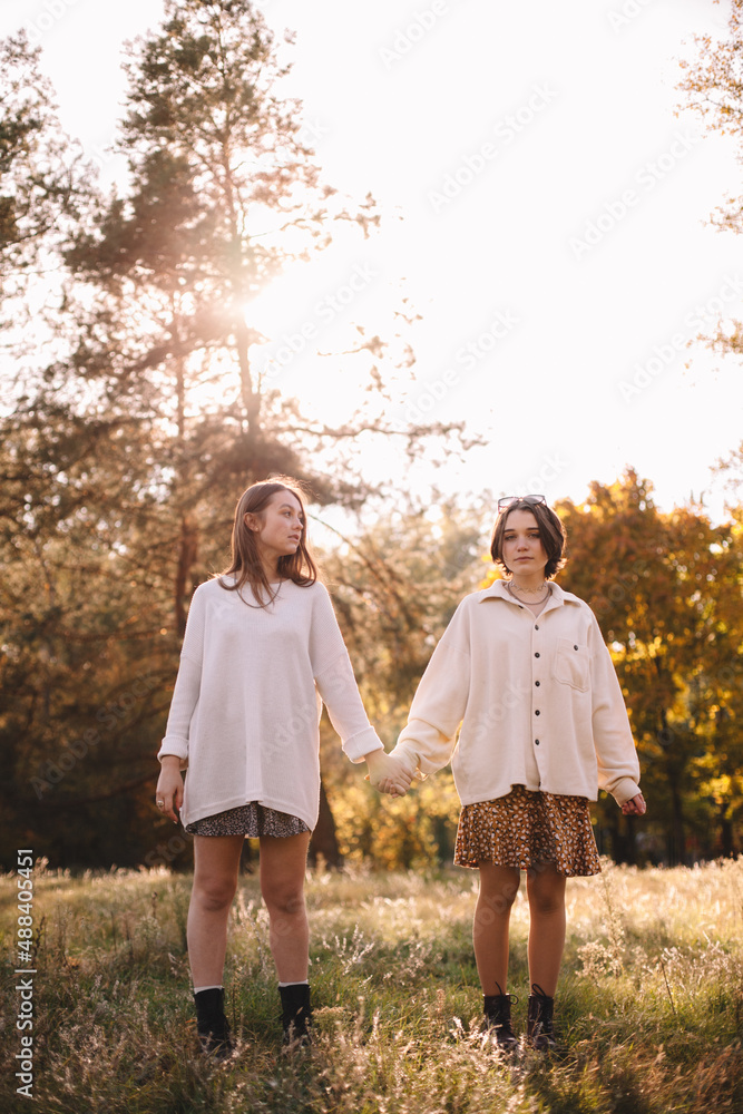 Lesbian couple holding hands while standing in forest during autumn Lesbian couple holding hands while standing in forest during autumn