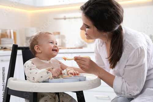 Foto Mother feeding her cute little baby in kitchen