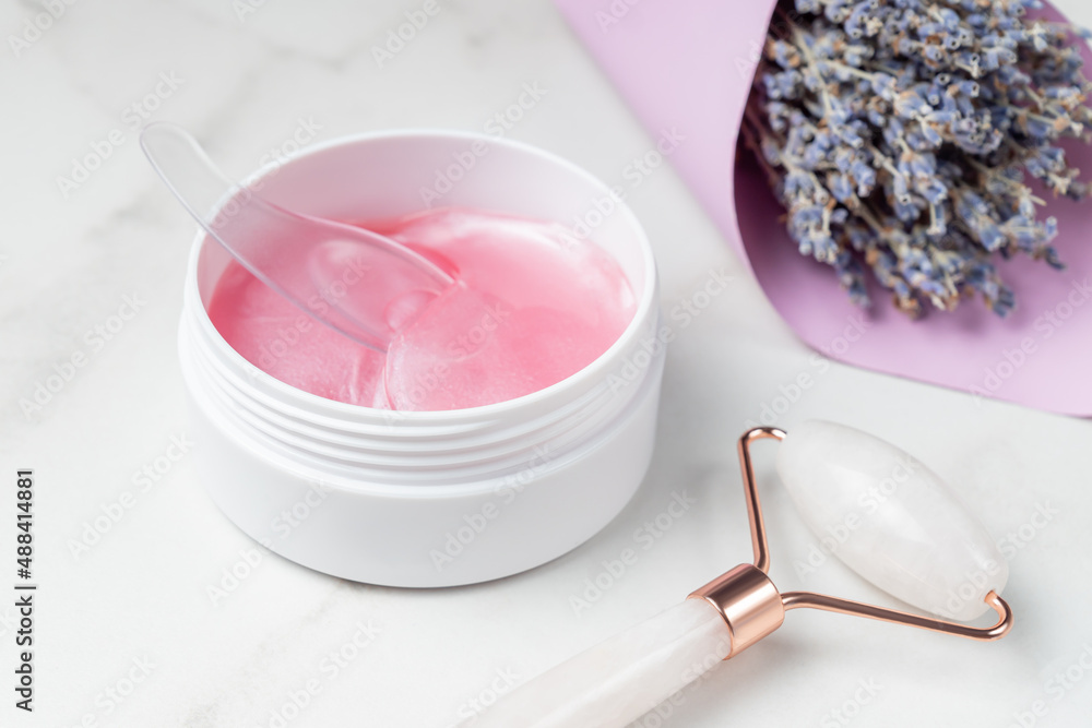 Pink hydrogel patches for skin under the eyes and rose quartz massage face roller on a table. Skin care home routine. Professional spa salon at home. Pink hydrogel patches for skin under the eyes and rose quartz massage face roller on a table. Skin care home routine. Professional spa salon at home.