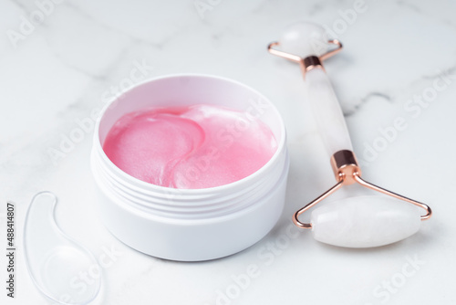 face massager roller made from natural stone and pink eye patches on marble background. Skin care treatment