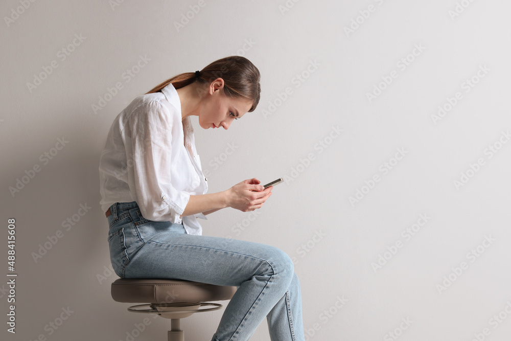 Woman with bad posture using smartphone while sitting on stool against light grey background, space for text Woman with bad posture using smartphone while sitting on stool against light grey background, space for text