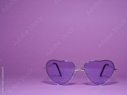 Heart shaped purple sun glasses on the purple background. A mysterious stranger. Holiday trip. Place for text