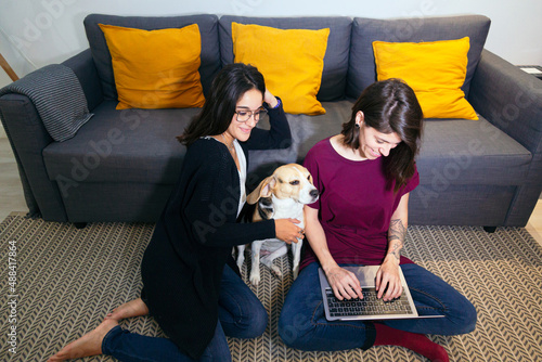 lesbian couple sitting in the living room looking at the laptop with the dog