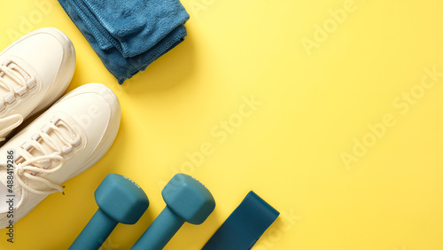 Fototapeta Naklejka Na Ścianę i Meble -  Fitness equipment for workouts on yellow background, top view. Flat lay feminine sport shoes, towel, dumbbells, fitness tape