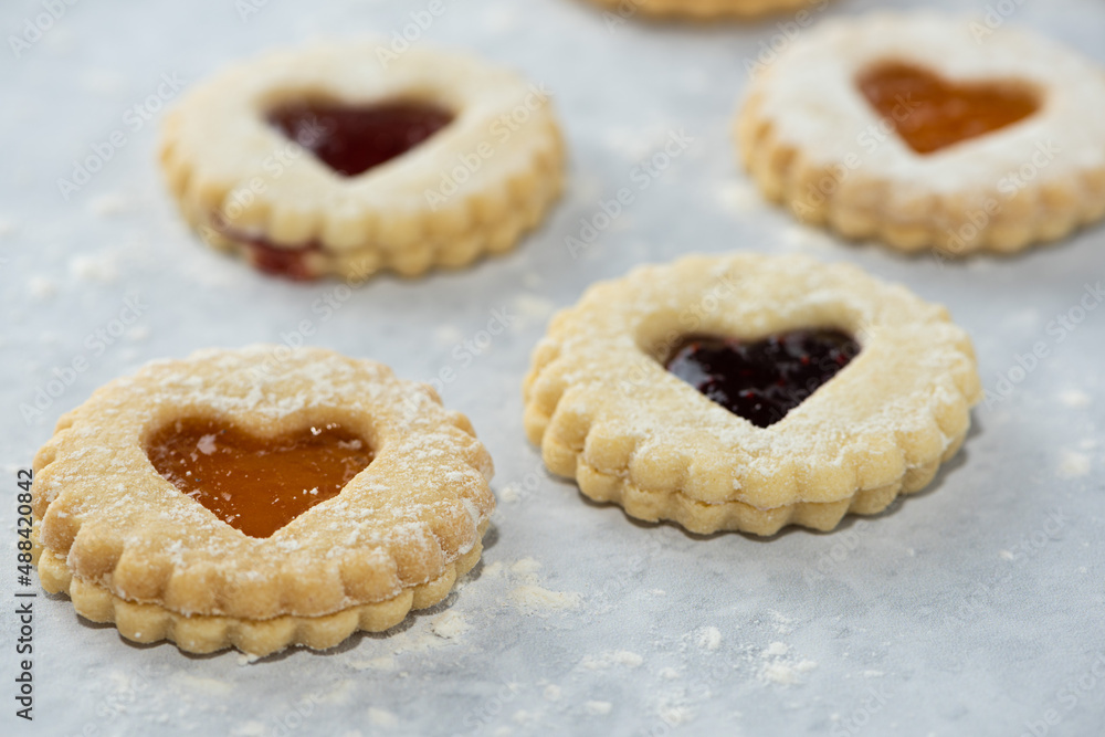 Elevated front view of homemade heart shaped jam filled holiday or celebration cookies with scattered flower on a marble table. Elevated front view of homemade heart shaped jam filled holiday or celebration cookies with scattered flower on a marble table.
