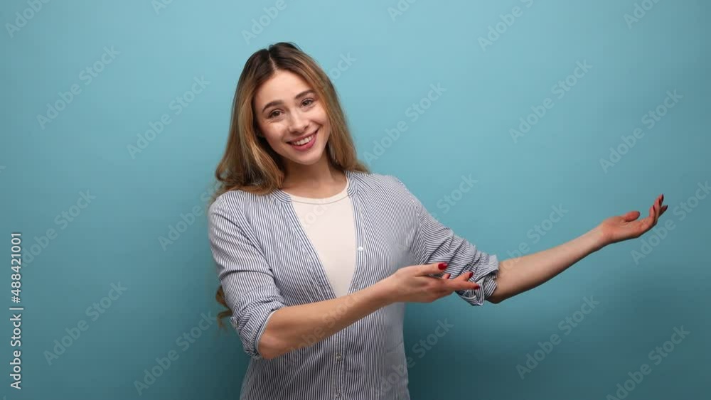 Portrait of smiling beautiful woman spreading her arms welcoming dear guests, greeting, inviting to come in, wearing striped shirt. Indoor studio shot isolated on blue background. Portrait of smiling beautiful woman spreading her arms welcoming dear guests, greeting, inviting to come in, wearing striped shirt. Indoor studio shot isolated on blue background.