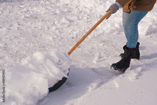 Snow removal in winter. A woman cleans the snow with a shovel in the local area. Woman clearing snow from her front yard. © Trik