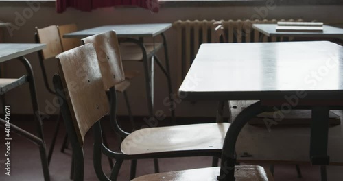 In an empty abandoned classroom with rows of desks and chairs, the camera moves around a desk, it’s a vintage east Germany school from the 70’s  to 80’s
