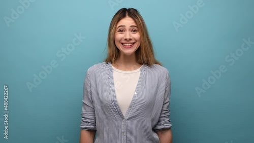 Positive optimistic woman looking at camera and nodding yes, showing approving gesture, body language concept, wearing striped shirt. Indoor studio shot isolated on blue background.