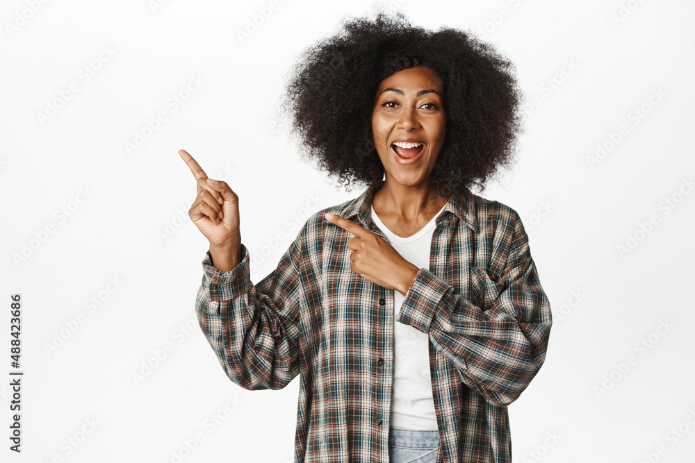 Smiling Black female model with afro hair, african woman pointing fingers left and smiling, showing information, points at announcement, white background Smiling Black female model with afro hair, african woman pointing fingers left and smiling, showing information, points at announcement, white background