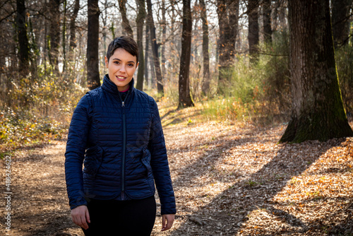 Young smiling woman is walking in the woods. Beautiful woman with short hair is walking in the park while she looks into the camera. Copy spase for your message. photo