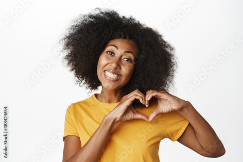 Love, relationship and valentines day. Beautiful african woman shows heart gesture and smiles, I like you gesture, express sympathy, white background