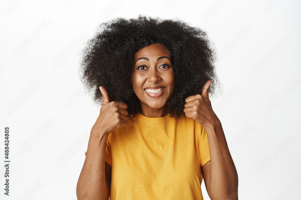 Very good, great job. Smiling happy african woman shows thumbs up, like gesture, recommending smth, praising and complimenting, standing over white background Very good, great job. Smiling happy african woman shows thumbs up, like gesture, recommending smth, praising and complimenting, standing over white background