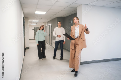 Woman in suit talking to couple in new building. Real estate agent showing building for sale. Couple with real estate agent visiting property for viewing.