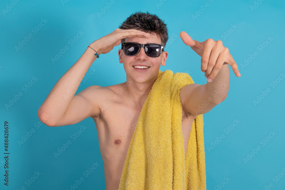 young man with sunglasses and towel smiling isolated with surfer gesture