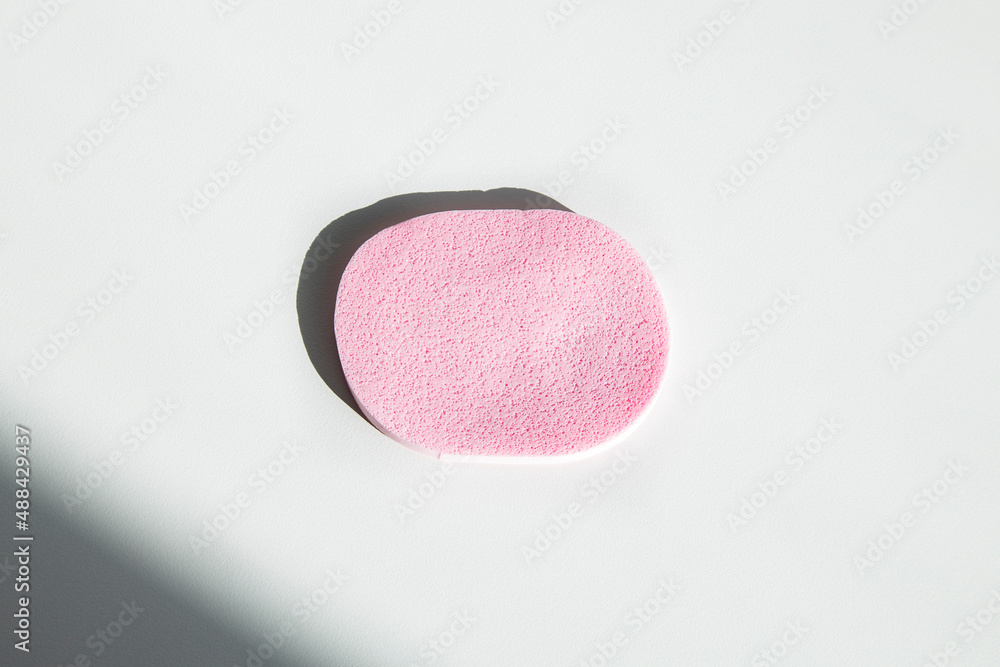 Pink sponge for makeup on a white table under the rays of the sun. Flat lay, top view Pink sponge for makeup on a white table under the rays of the sun. Flat lay, top view