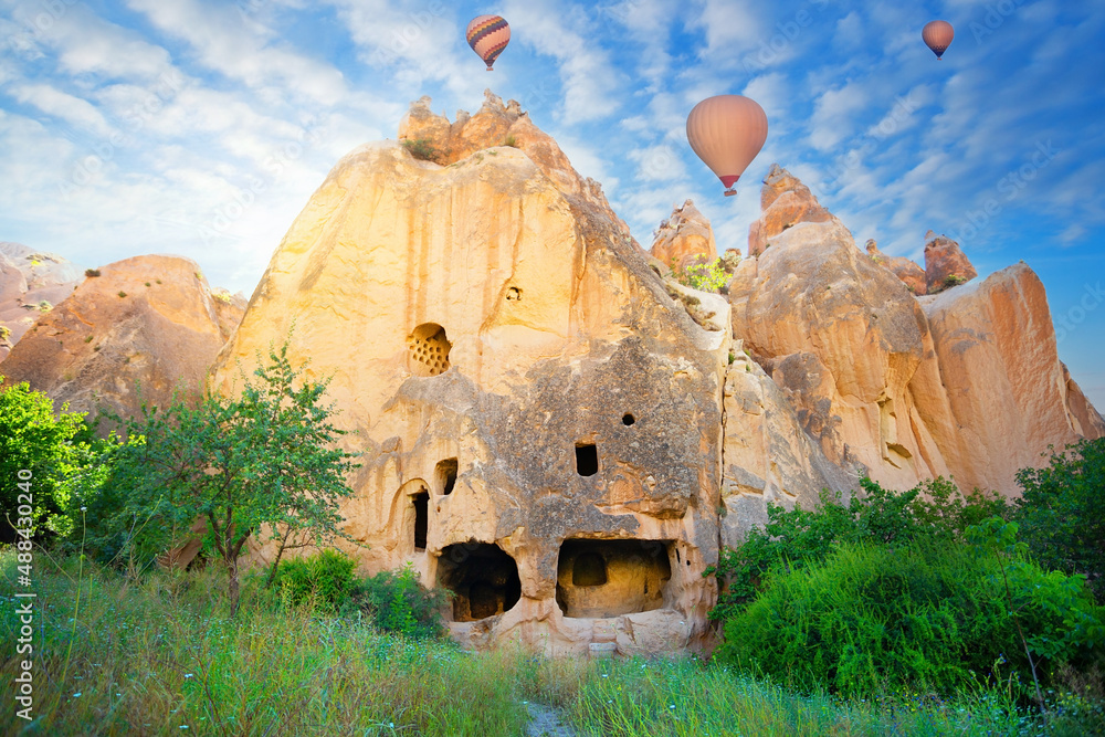 Rock monastery in the Zelve valley under blue sky with hot air balloons - obrazy, fototapety, plakaty 