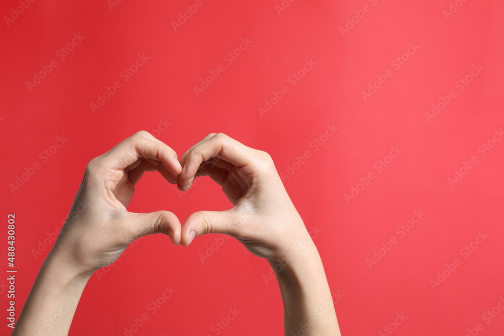 Obraz premium Woman making heart with her hands on red background, closeup. Space for text