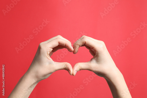 Woman making heart with her hands on red background, closeup