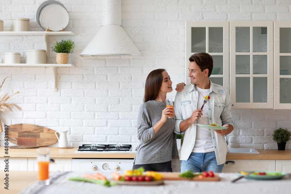 Beautiful young couple looks at each other and smiles while eating in the kitchen. Healthy eating Beautiful young couple looks at each other and smiles while eating in the kitchen. Healthy eating