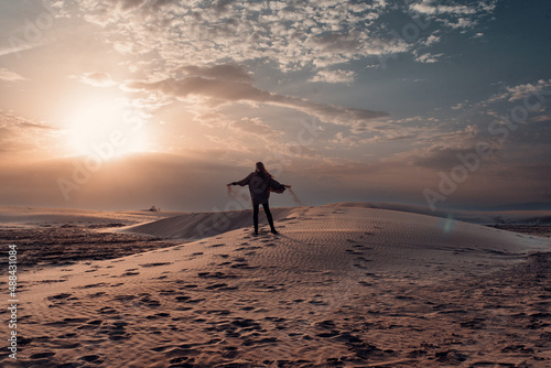 Woman dropping sand from her hands on the dunes of a beach at sunset.