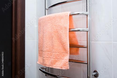 orange terry towel hanging on a chrome heated towel rail in the bathroom photo