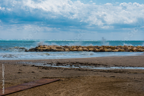 Surf at the breakwater on the sea, rain clouds in blue sky