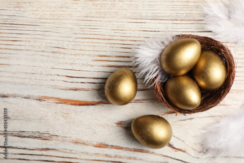 Nest with golden eggs on white wooden table, flat lay. Space for text