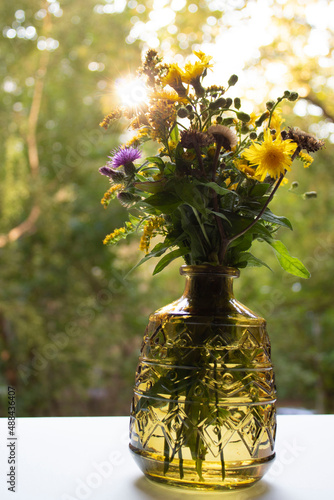 Bouquet of dandelions, thistles and dried flowers. Beautiful glass vase on the windowsill on a sunny day.