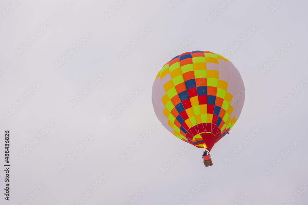 Fototapeta premium Colorful hot air balloon flying against grey sky at Winter aerostat festival, snow falling. Freedom, sport, aircraft concept