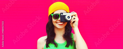 Summer colorful portrait of happy smiling young woman photographer taking pictures with camera on pink background, blank copy space for advertising text