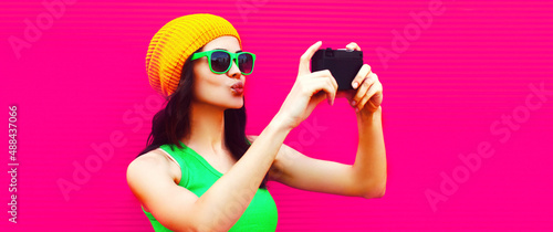 Summer colorful portrait of happy modern young woman taking selfie by camera on pink background