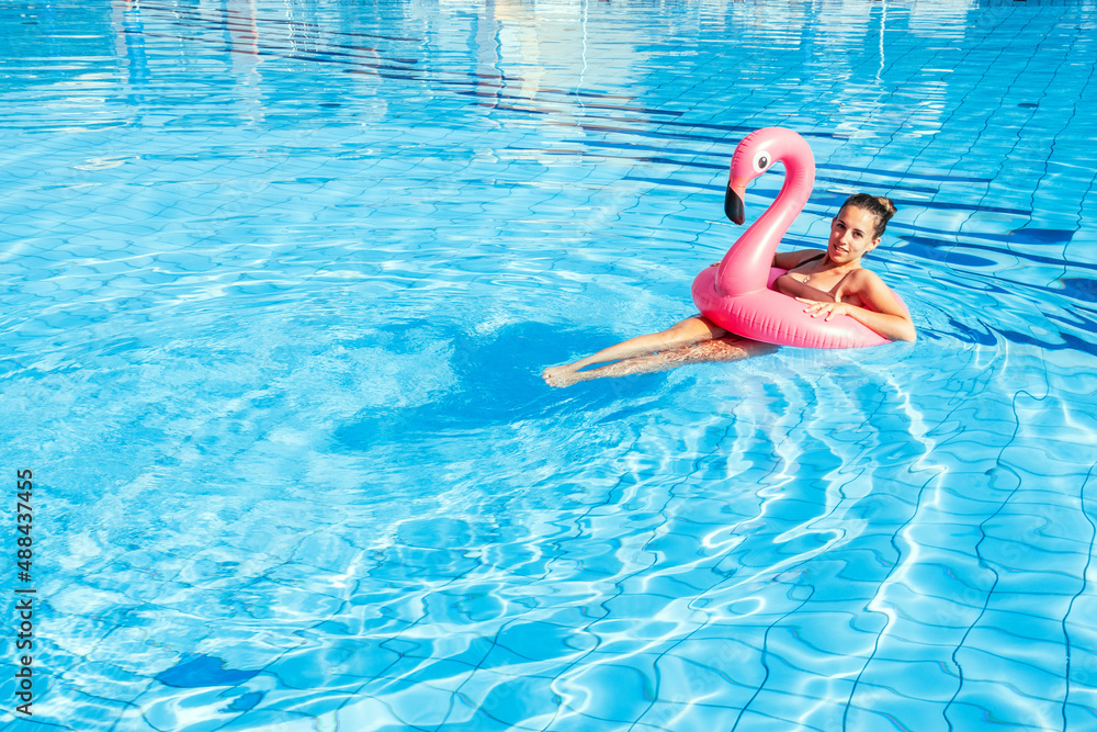 Summer pool relaxing. Young sexy woman in bikini swimsuit float with pink flamingo in blue water. Trendy summer concept.