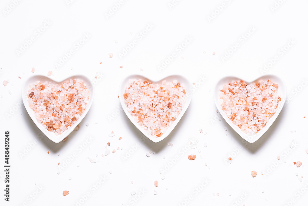 Three heart-shaped bowls with pink Himalaya salt on white background top view. 