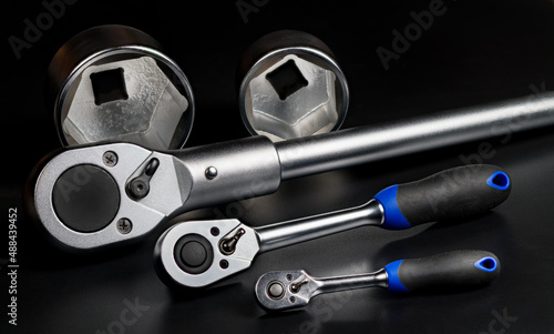 Closeup of metal ratchets and interchangeable hex sockets on black background. Three sizes of steel ratcheting socket wrenches with plastic grip and two different replaceable hexagon tightening tools. photo