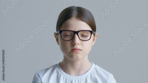 Blonde teenager girl in a white T-shirt puts on red glasses against a white wall