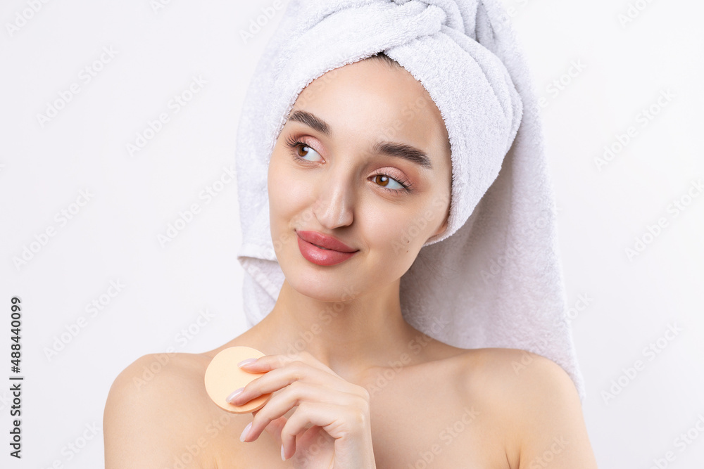 Beautiful girl with thick eyebrows and perfect skin at white background, towel on head, beauty photo. Holds a cosmetic sponge. Beautiful girl with thick eyebrows and perfect skin at white background, towel on head, beauty photo. Holds a cosmetic sponge.