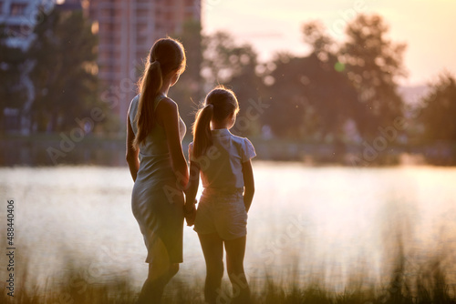 Happy mother and daughter standing together looking at building under construction dreaming about their future home at sunset. Family love and relationship concept