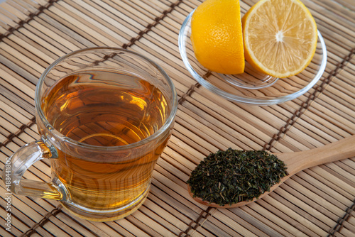 Cup of green tea, lemon slices, dry leaves on a wicker