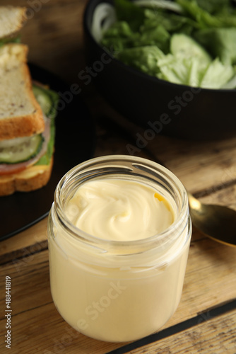 Jar of delicious mayonnaise near fresh sandwiches on wooden table