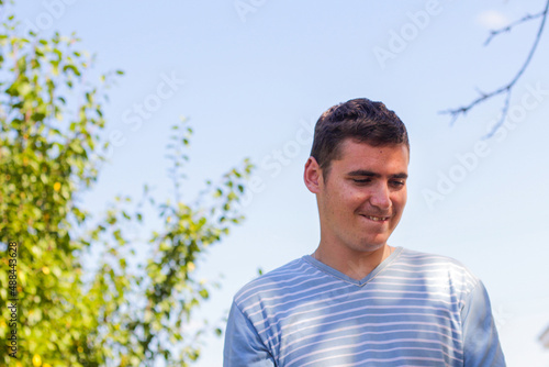 Defocused young caucasian man looking conspiracy. Summer outdoor blue sky and green tree background. Out of focus