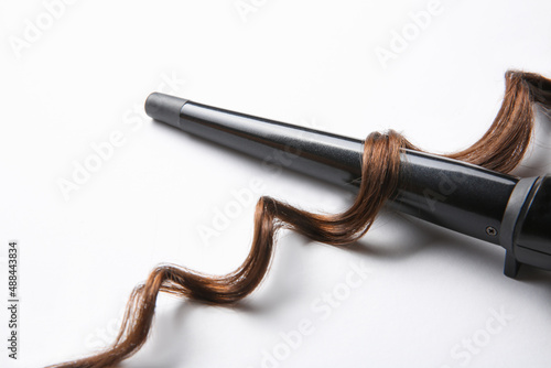 Foto Modern clipless curling iron and brown hair lock on white background