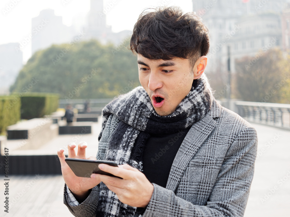 Happy excited young man in suit using cell phone with funny expression, excited business man looking at his smart phone reading good news message email or win in game, emotional lifestyle concept. Happy excited young man in suit using cell phone with funny expression, excited business man looking at his smart phone reading good news message email or win in game, emotional lifestyle concept.