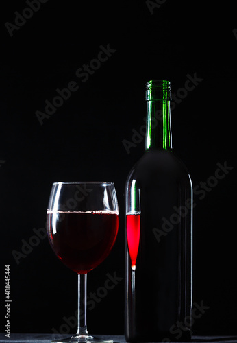 A glass of wine is reflected in the bottle on a dark background. The concept of drinking wine.