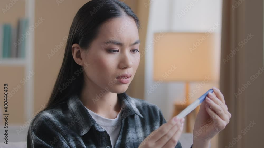 Unplanned children. Shocked pregnant asian korean young lady woman girl looking at positive pregnancy test result sitting at home worrying about having baby. Unwanted pregnancies reaction concept Unplanned children. Shocked pregnant asian korean young lady woman girl looking at positive pregnancy test result sitting at home worrying about having baby. Unwanted pregnancies reaction concept